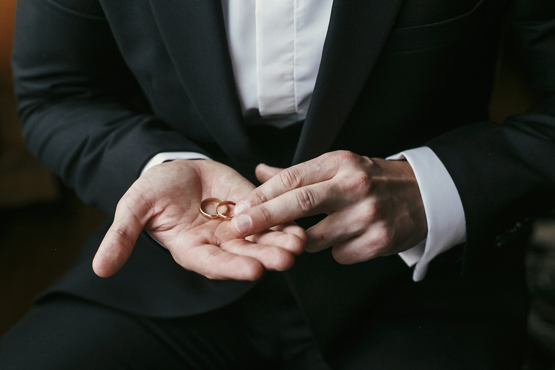 a groom holding two polished rose gold wedding bands in his hand