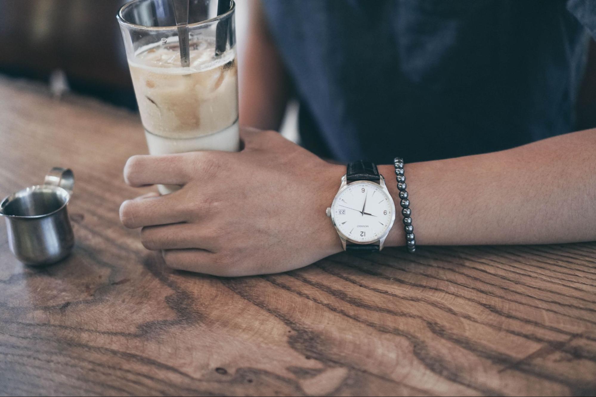 A close-up of a man’s wrist as he sits at a bar, wearing a minimalist watch and beaded bracelet.