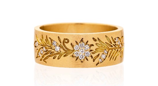 a yellow gold bangle with vine designs etched into it and diamond detail