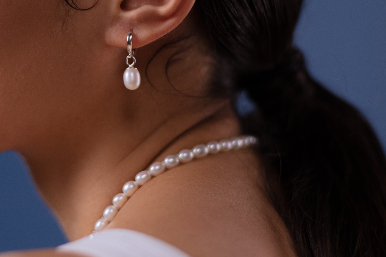 close up image of a woman’s neckline adorned with a pearl necklace and wearing a matching pearl earring