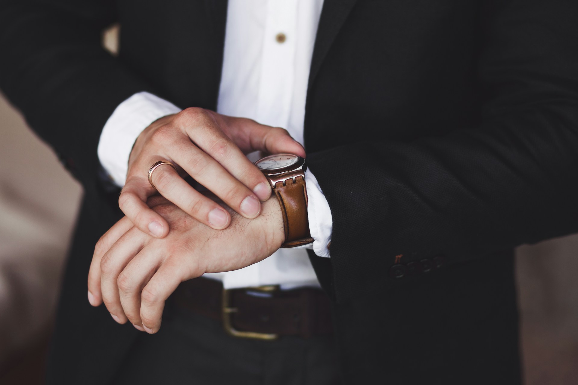 a man in a suit adjusting the brown leather strapped watch on his wrist