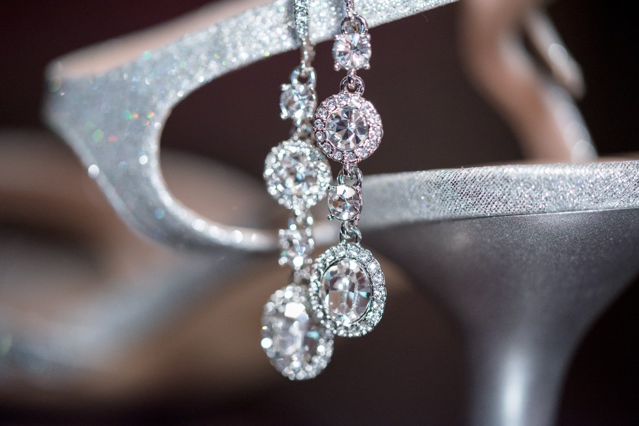 A close-up of a dazzling pair of diamond drop earrings displayed on an elegant shoe.