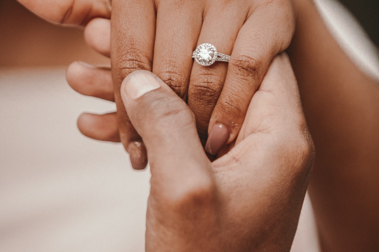 A woman wearing a split shank halo engagement ring holds a man’s hand.