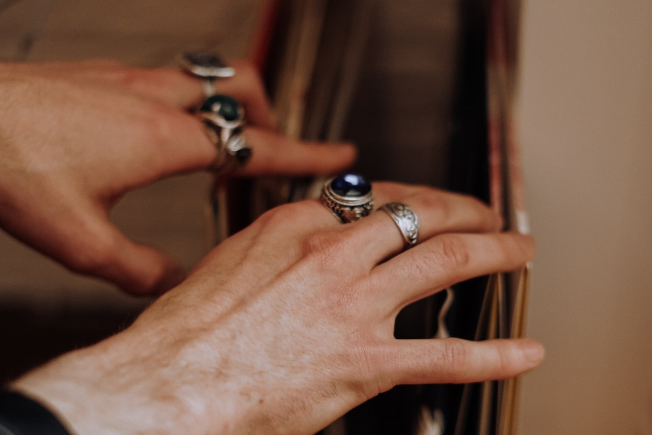 a person’s hands adorned with silver fashion rings, looking through records