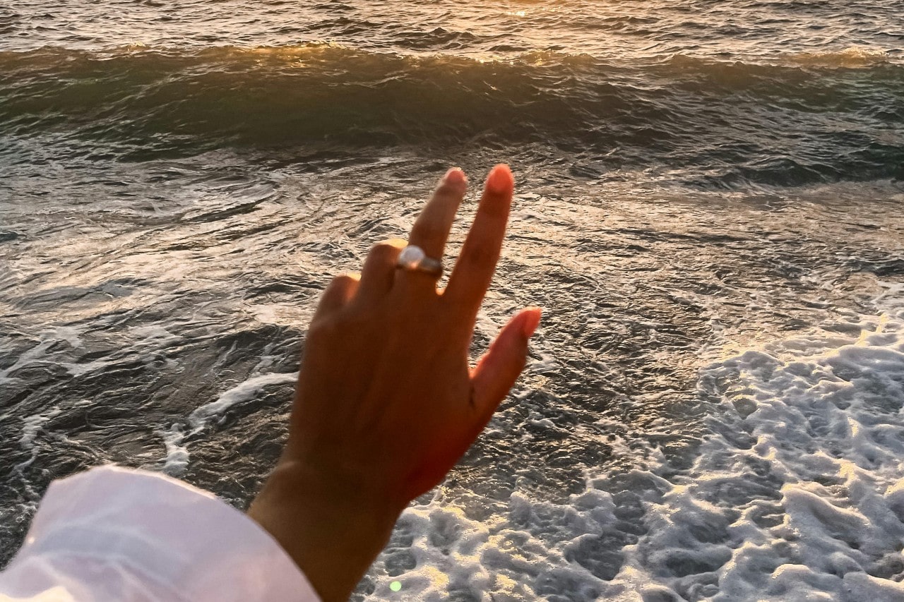 a woman’s hand extended in front of the sea, wearing a large pearl fashion ring