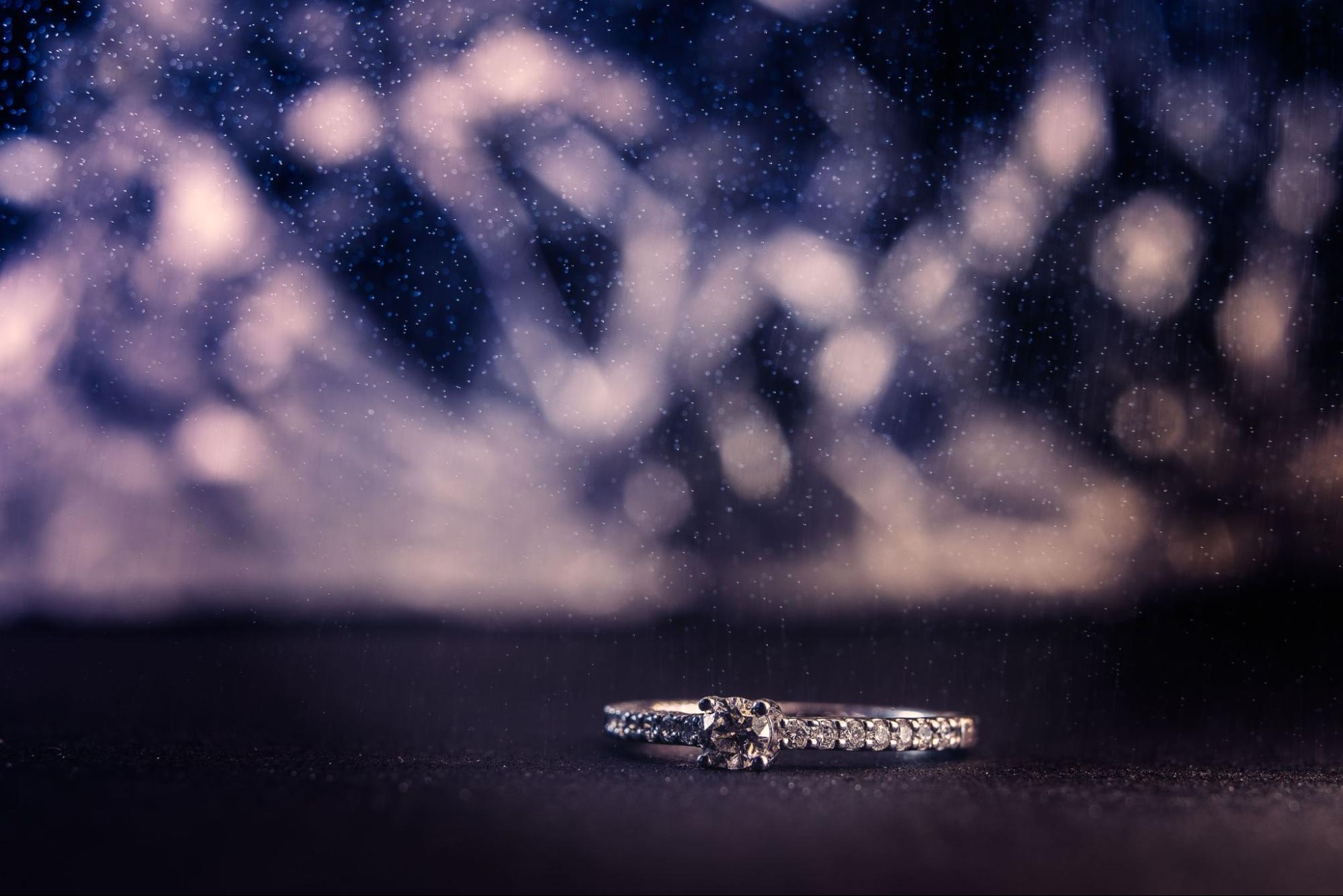 a white gold diamond side stone engagement ring lying on a dark surface with a sparkling background