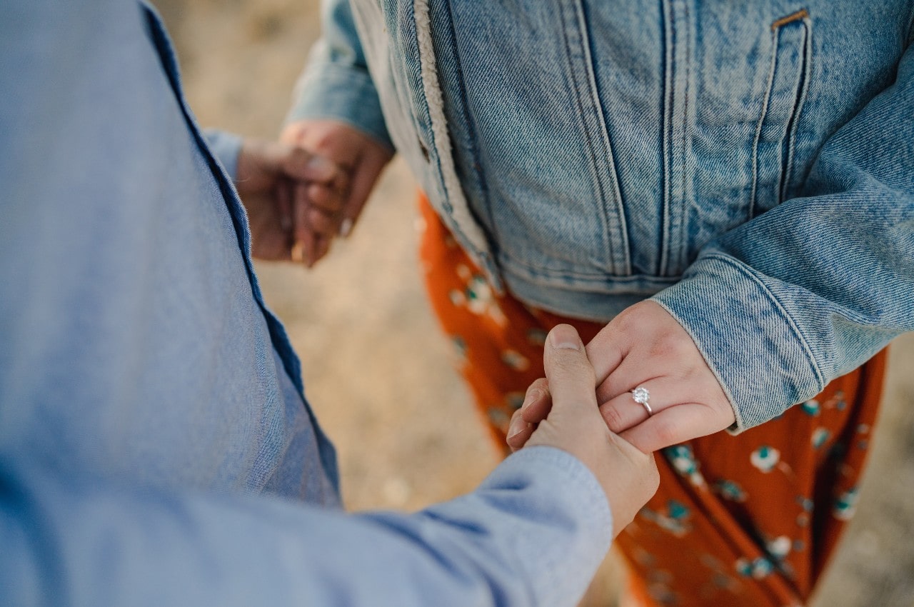 close up image of a man and woman holding hands–the woman wearing a diamond engagement ring